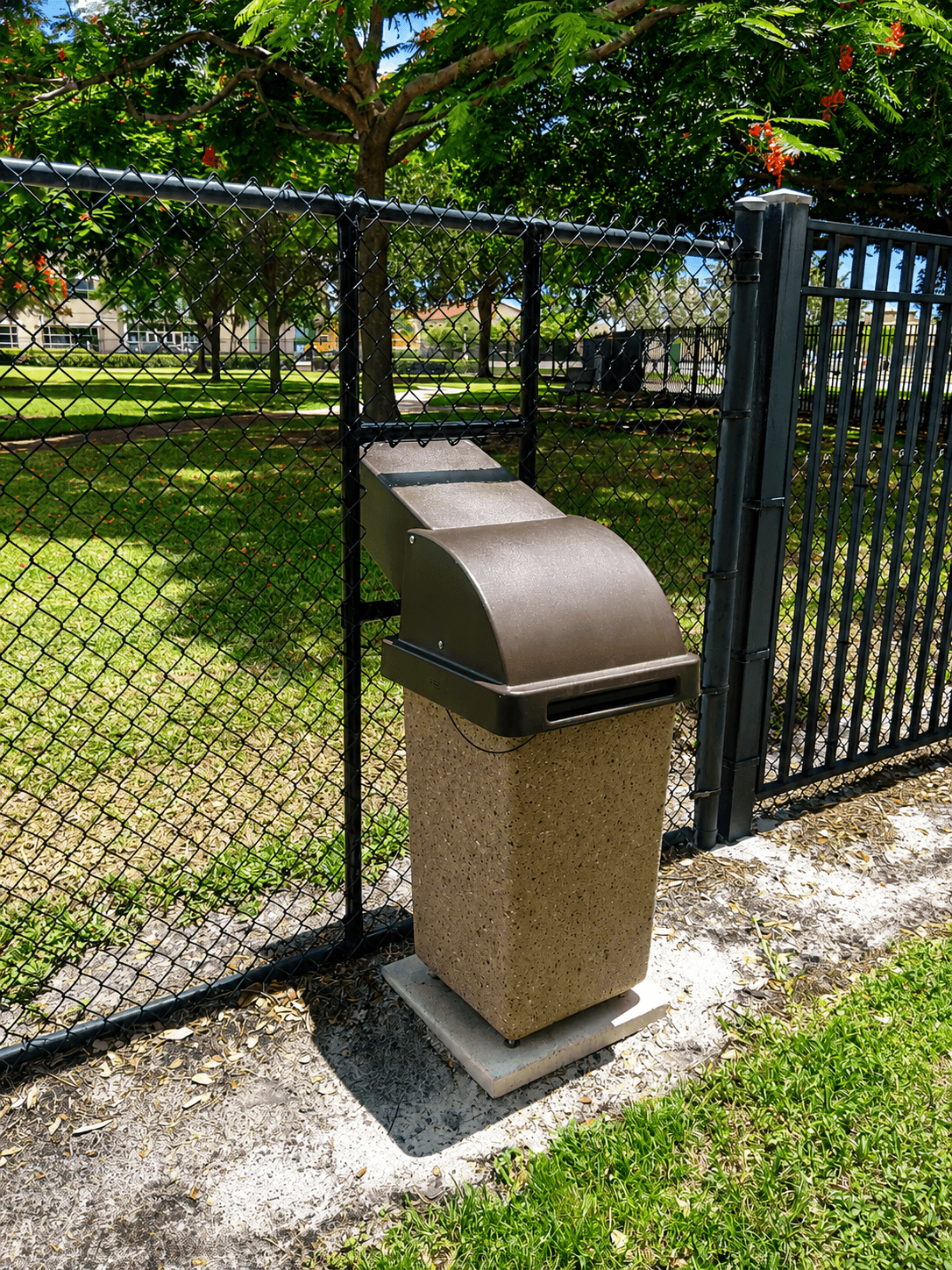 Black ornamental fence meeting chain link with integrated park trash receptacle