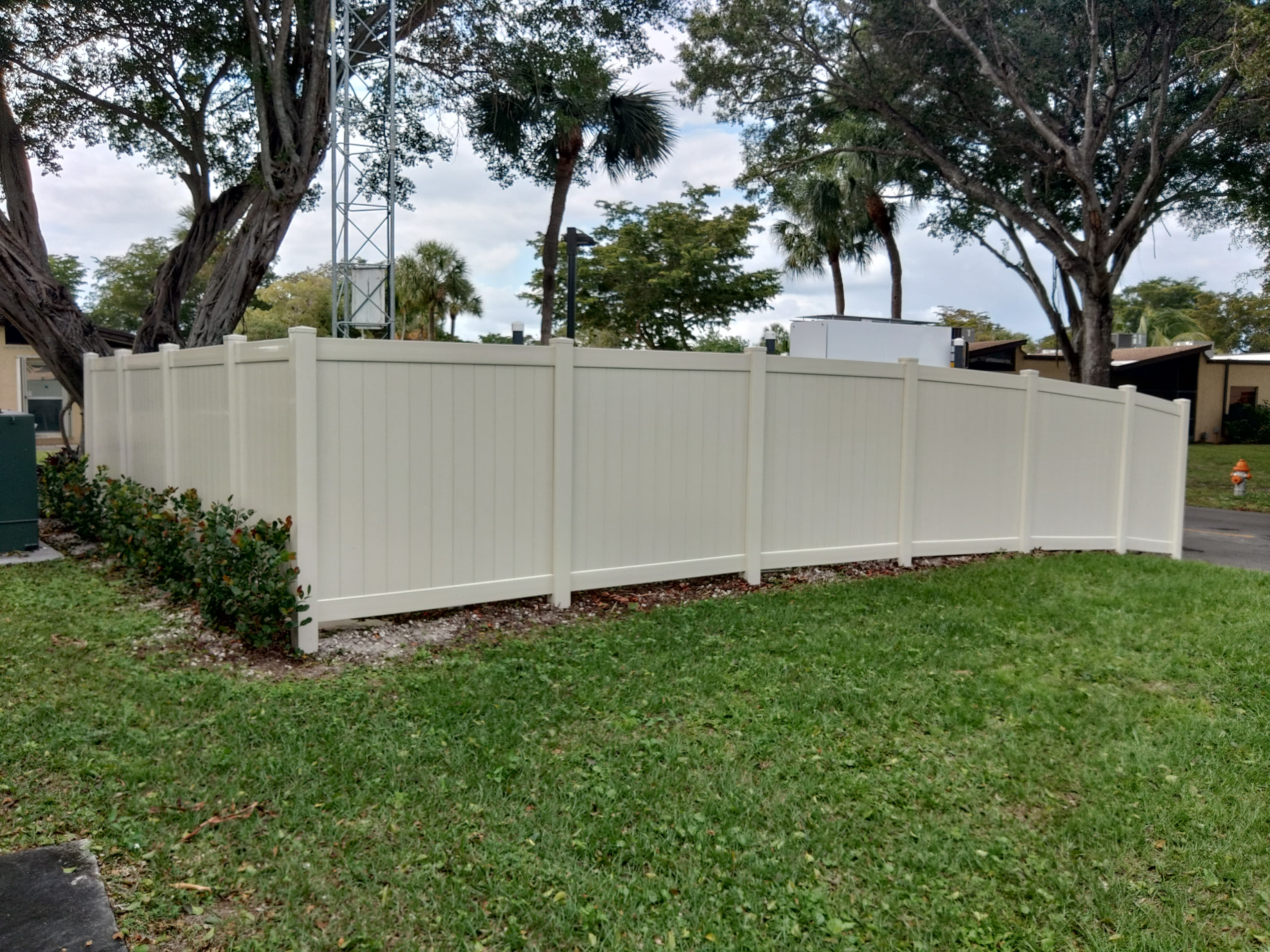 Long almond vinyl privacy fence along a landscaped commercial perimeter