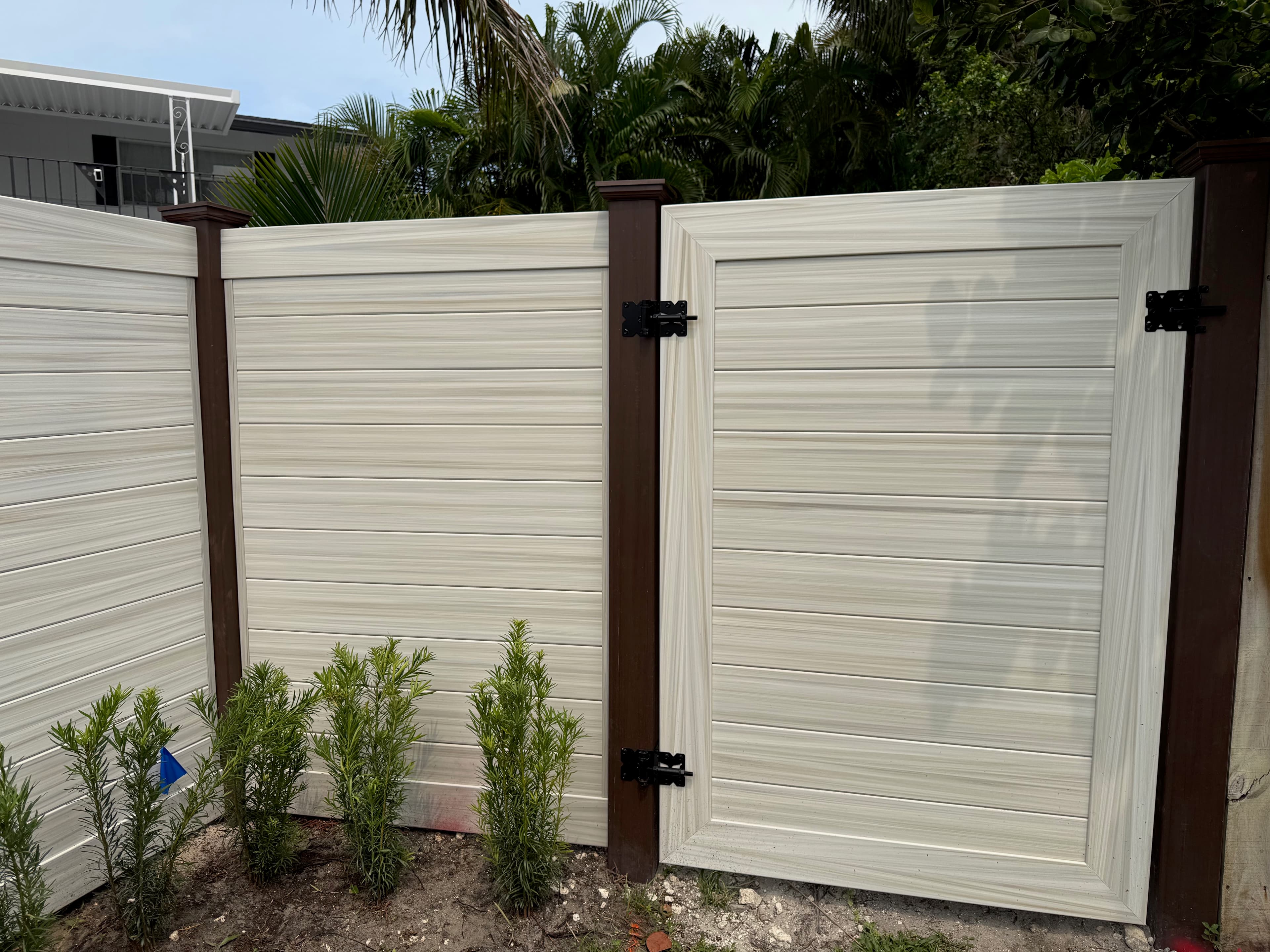 Two-tone horizontal privacy gate with black hinges and tropical landscaping