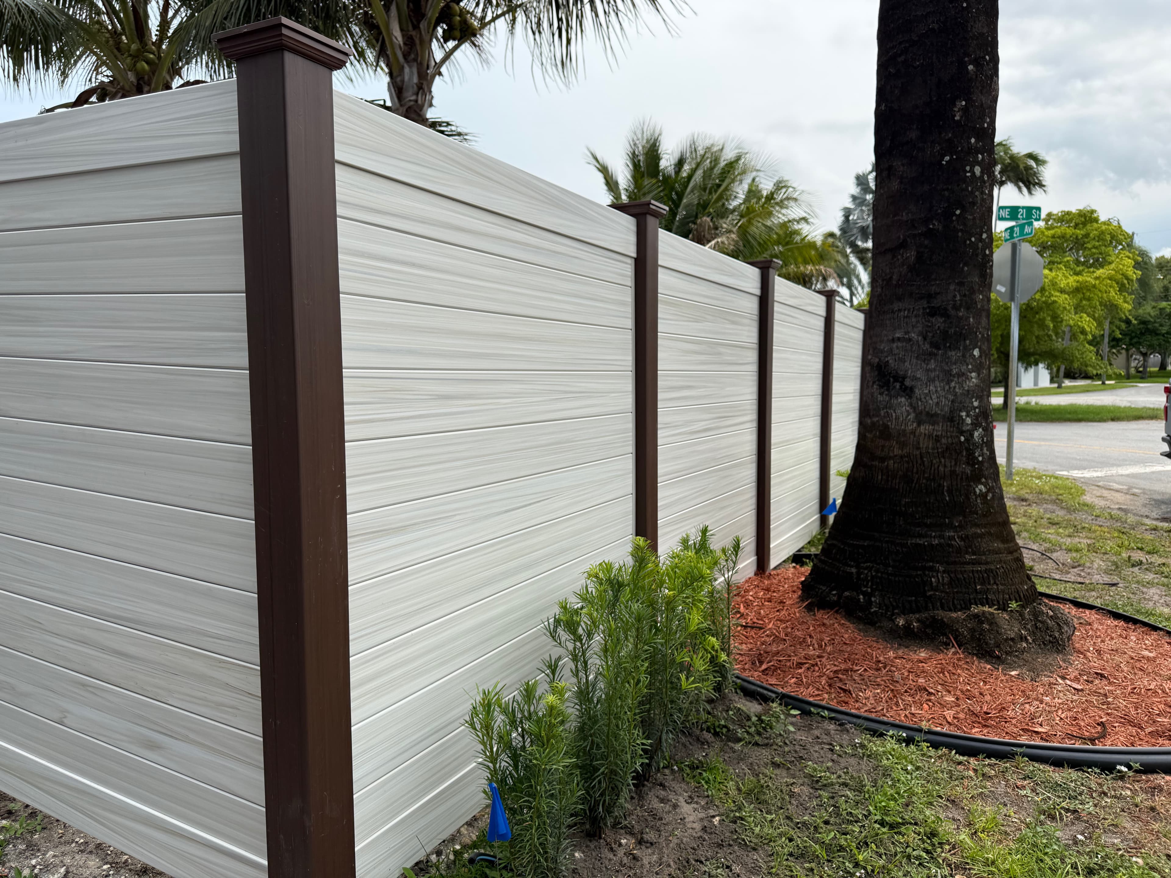Horizontal privacy fence at a street corner with palm trees and fresh mulch