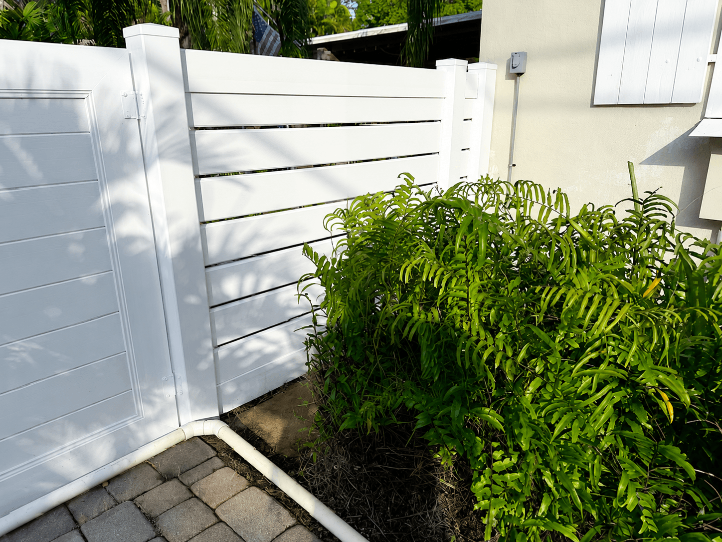 Semi-privacy white vinyl fence and gate beside a home exterior and fern bed