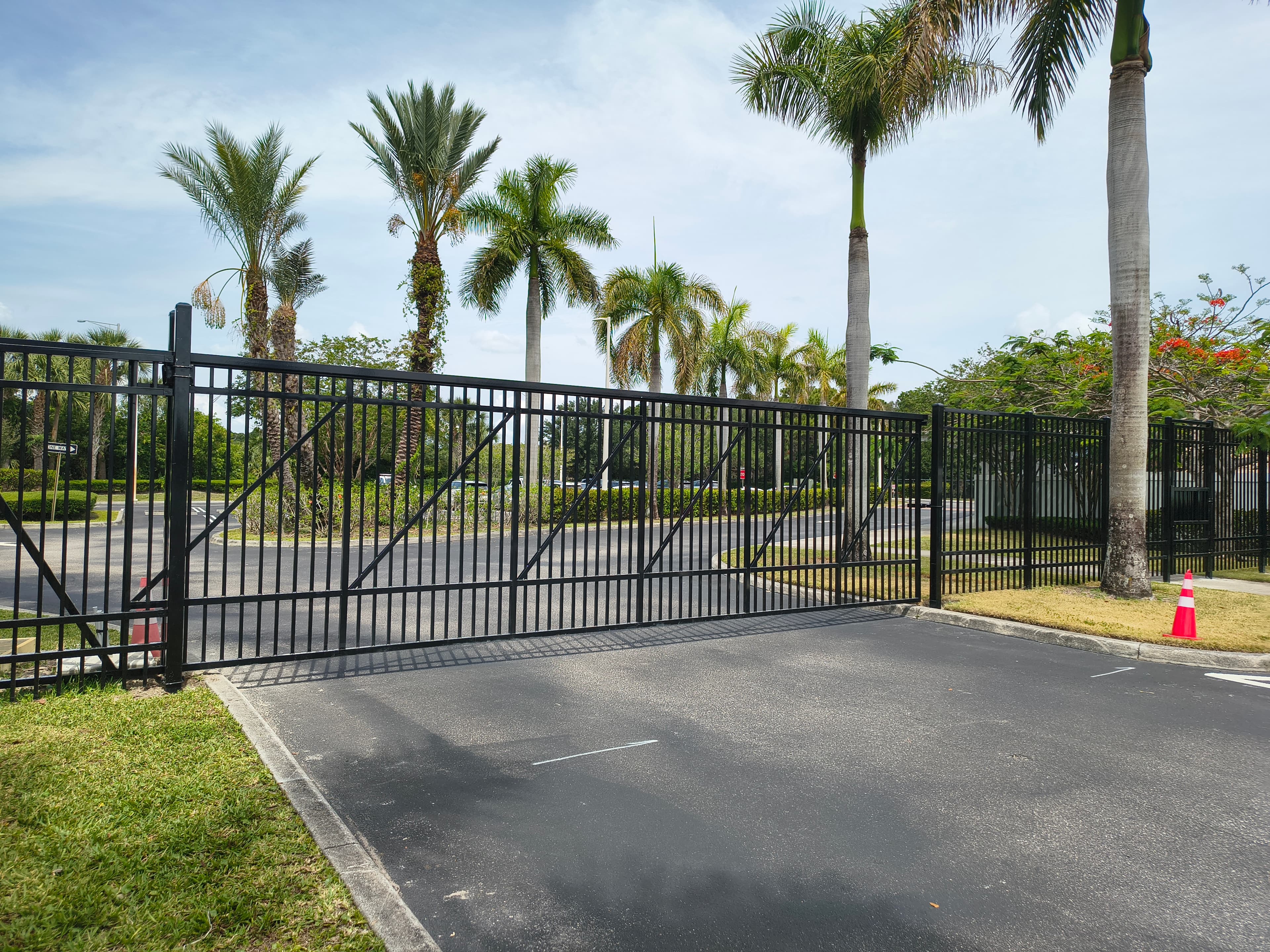 Black ornamental slide gate across a palm-lined property entrance drive