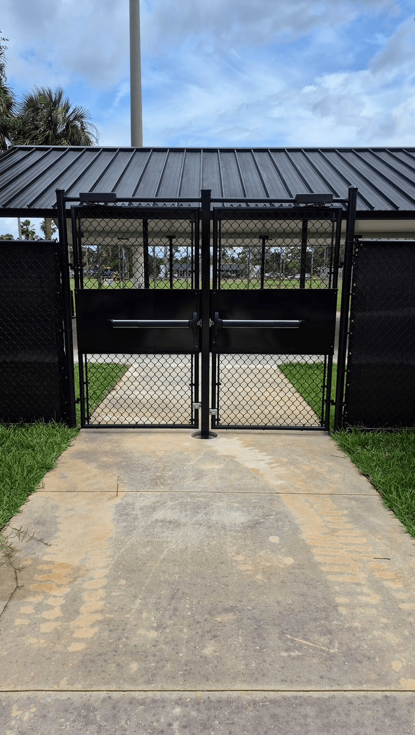 Black chain-link double gate with panic bars at a sports facility entrance