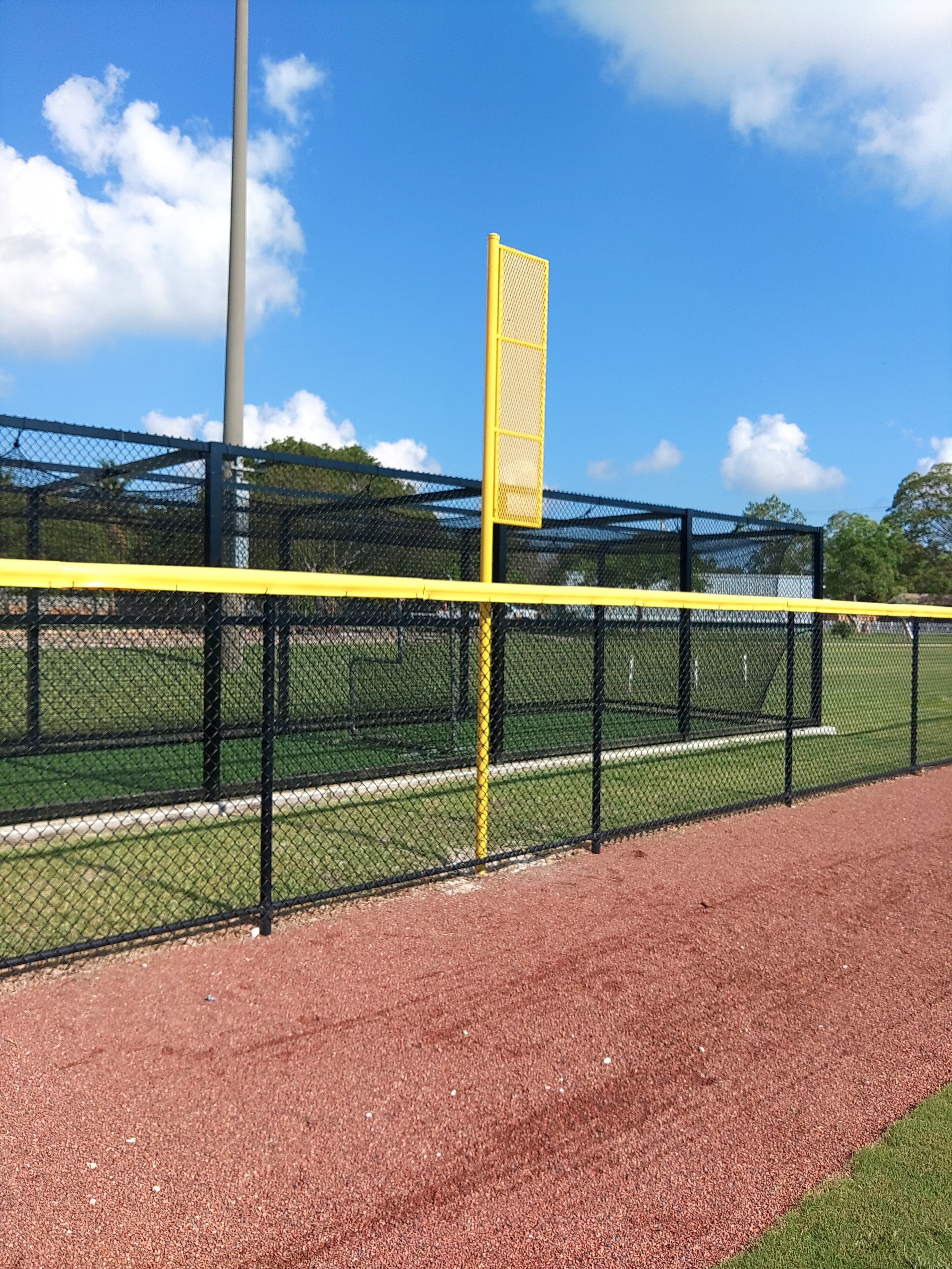 Yellow foul pole and chain link outfield fencing at a baseball field under a clear sky